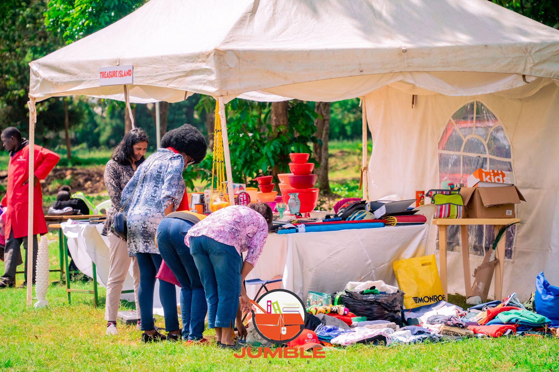 People browsing items at an outdoor market stall under a white tent with various goods displayed.