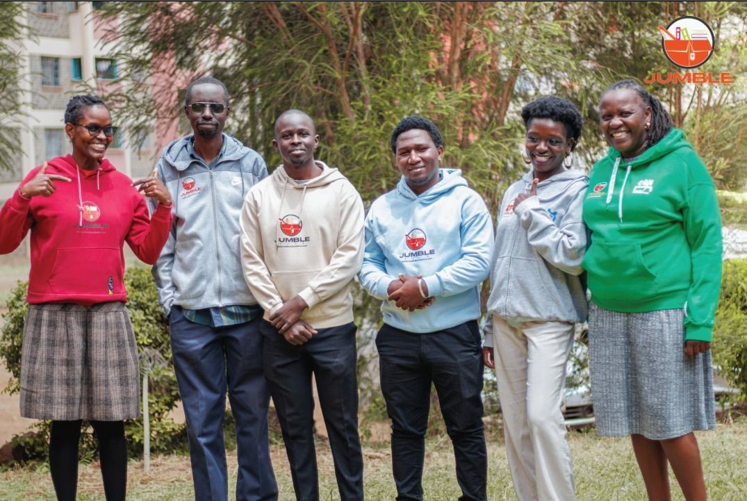 Group of six people smiling and wearing colorful Jumble hoodies, standing outdoors.