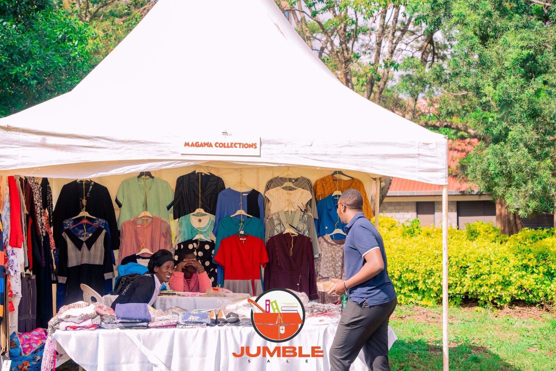 Outdoor market stall with hanging clothes and two people interacting.