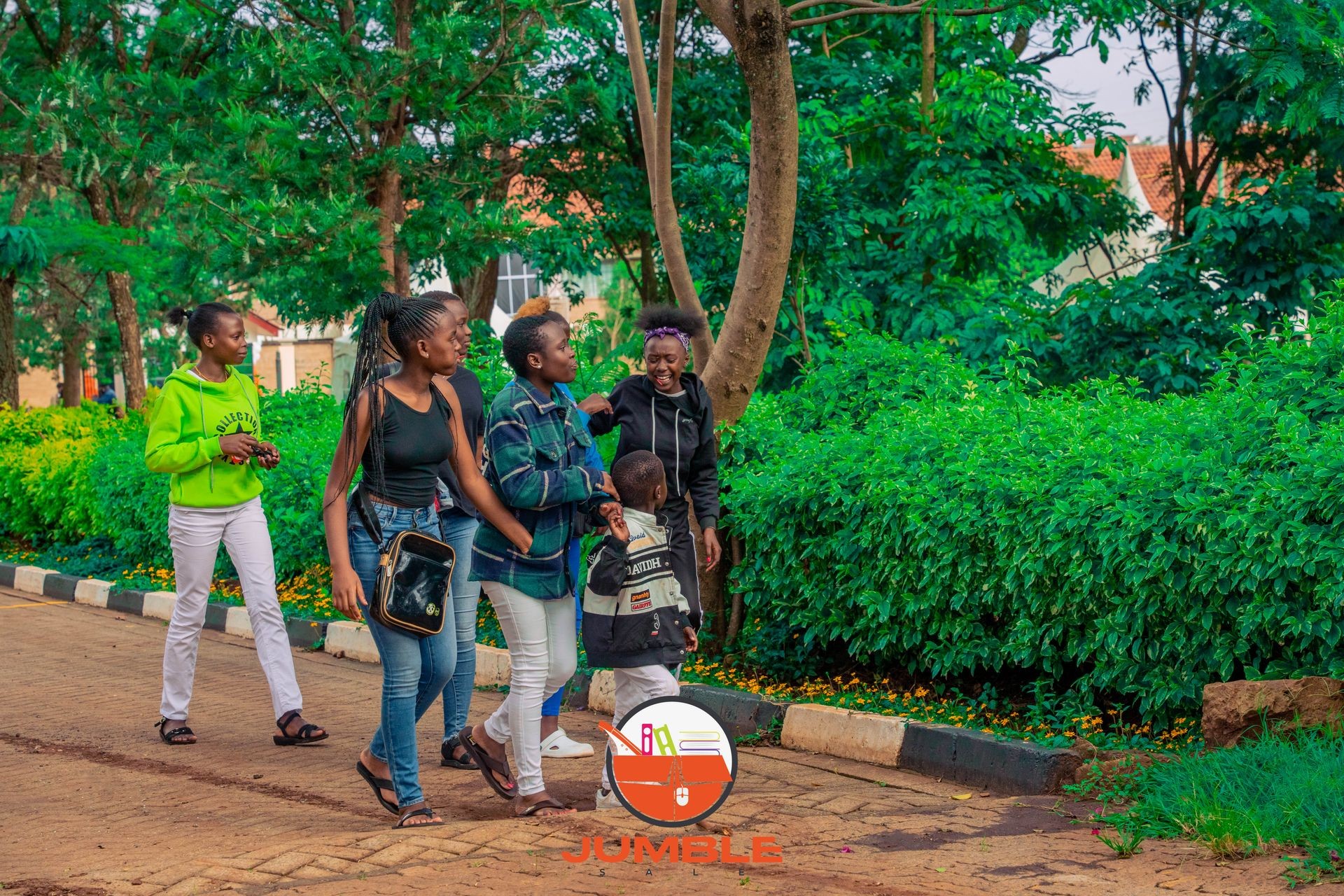 Group of people walking along a pathway with lush green bushes and trees in the background.